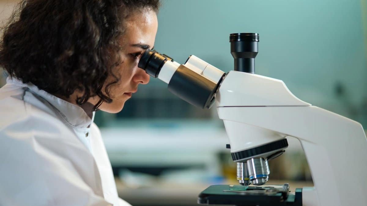 A focused scientist examines samples under a microscope in a laboratory setting.