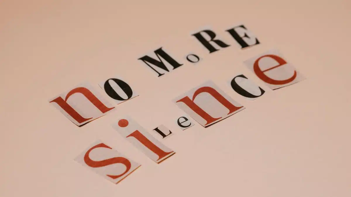 Typography artwork using cutout letters spells 'No More Silence' against a beige background.
