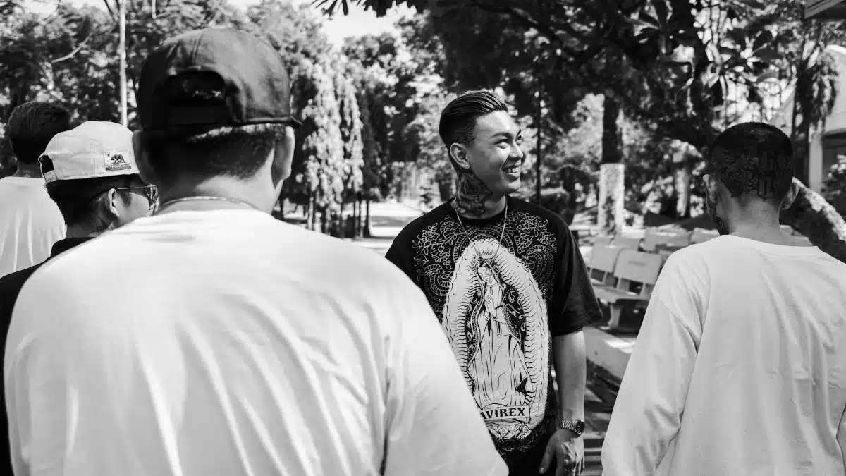Black and white happy Asian man with tattooed smiling and looking away while resting on street with friends