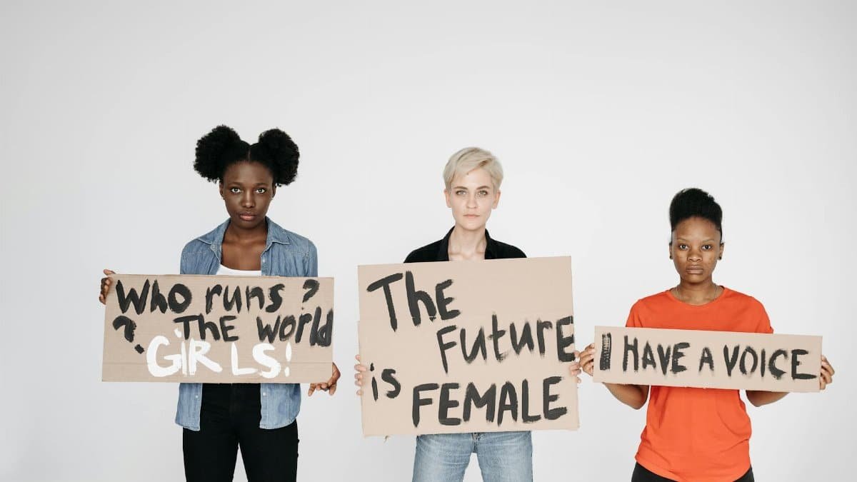 Three diverse women holding signs empowering female voices and rights.