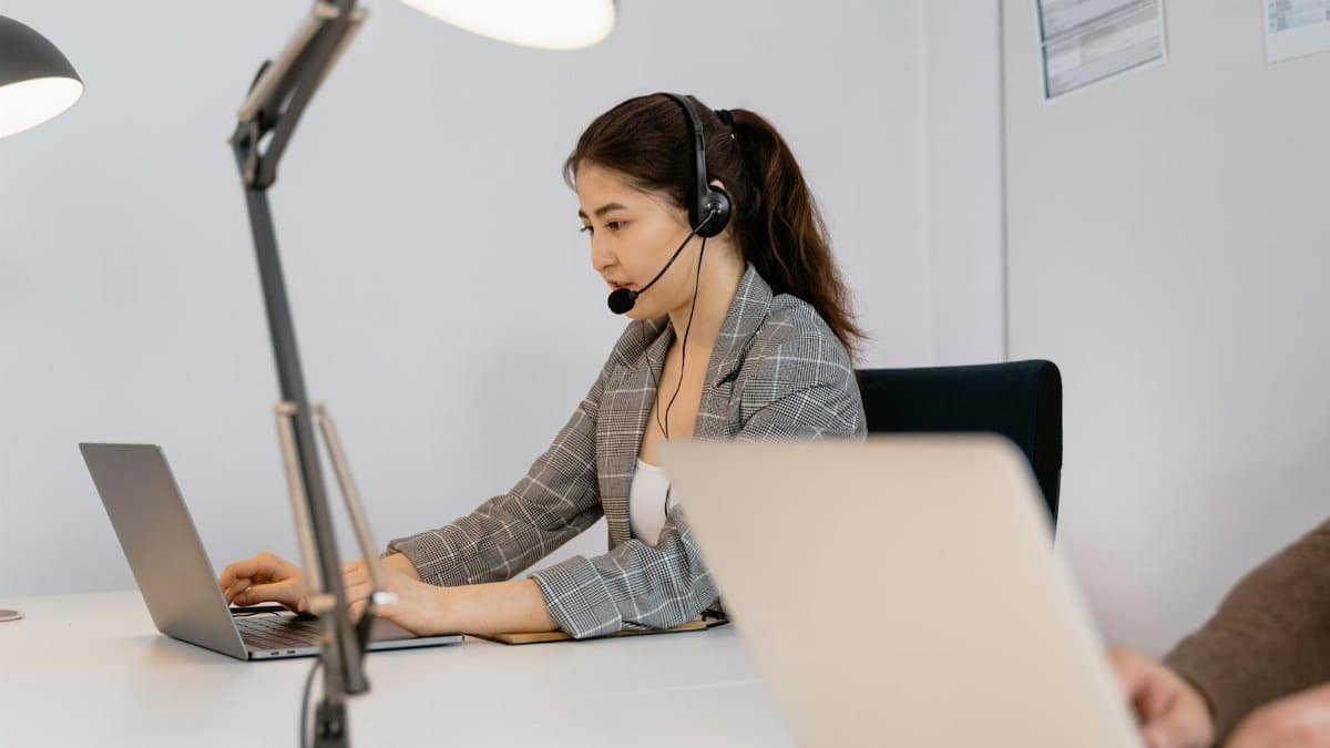 Focused woman at a desk with a headset, providing customer support in an office setting.