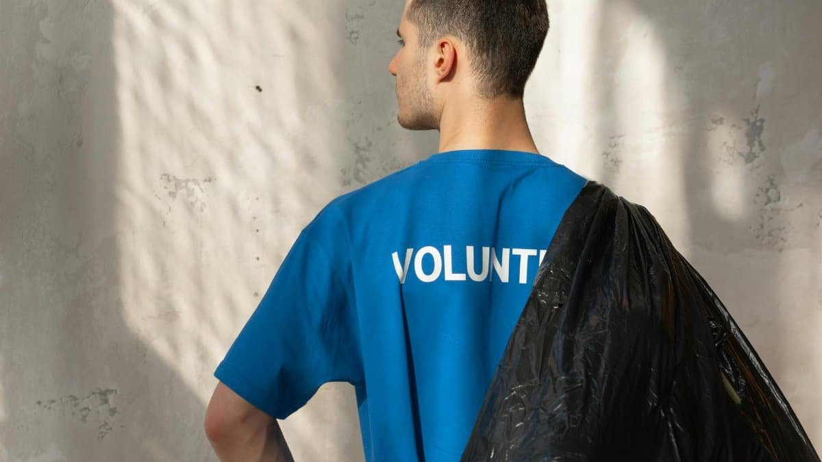Man in blue volunteer shirt holding garbage bag, symbolizing environmental conservation and cleanup efforts.