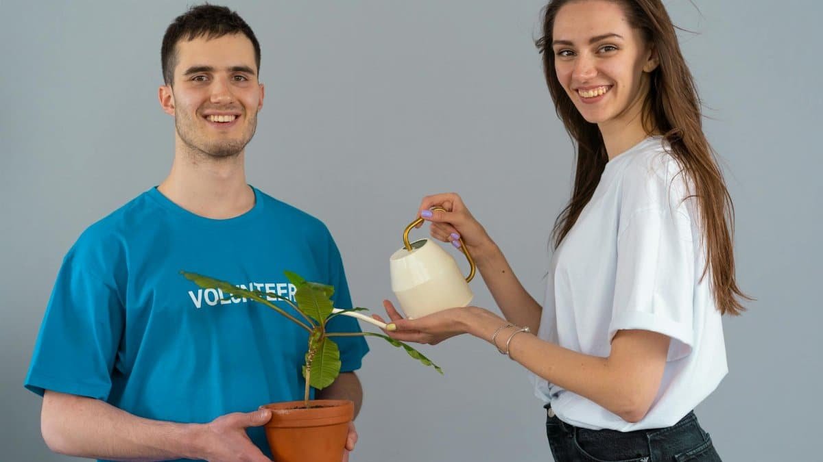 Two volunteers smiling while caring for a potted plant indoors, promoting teamwork and environmental care.