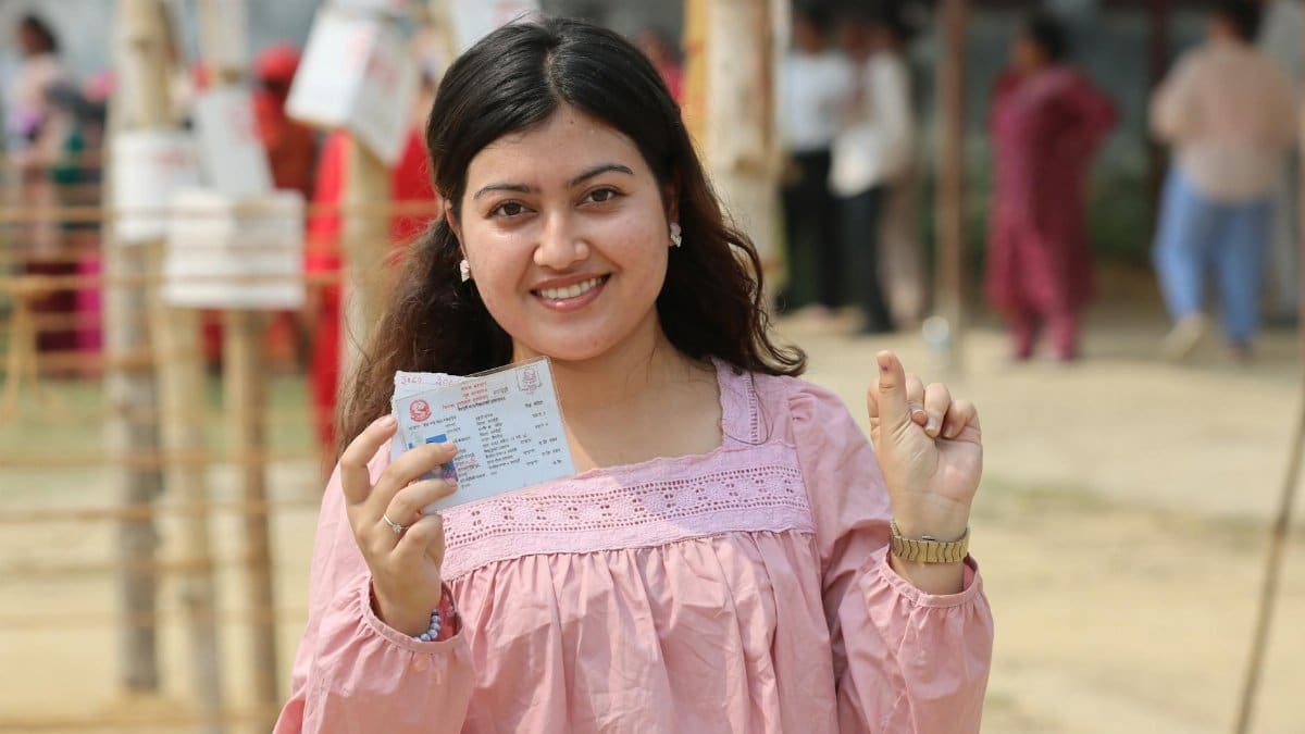 Young woman proudly displays voting ticket at outdoor polling station in Nepal.