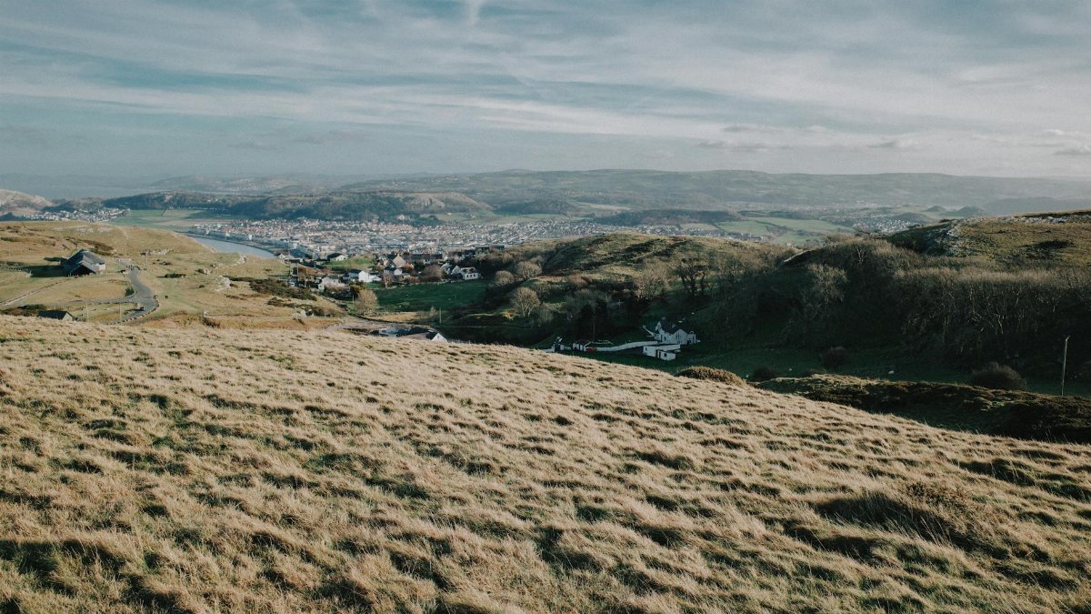 A breathtaking view of the rolling hills and a picturesque town in Wales under a clear sky.