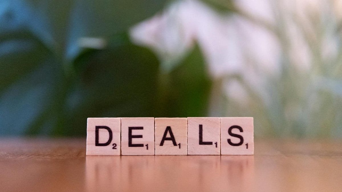 Close-up of Scrabble tiles spelling 'DEALS' on a wooden surface with blurry green background.