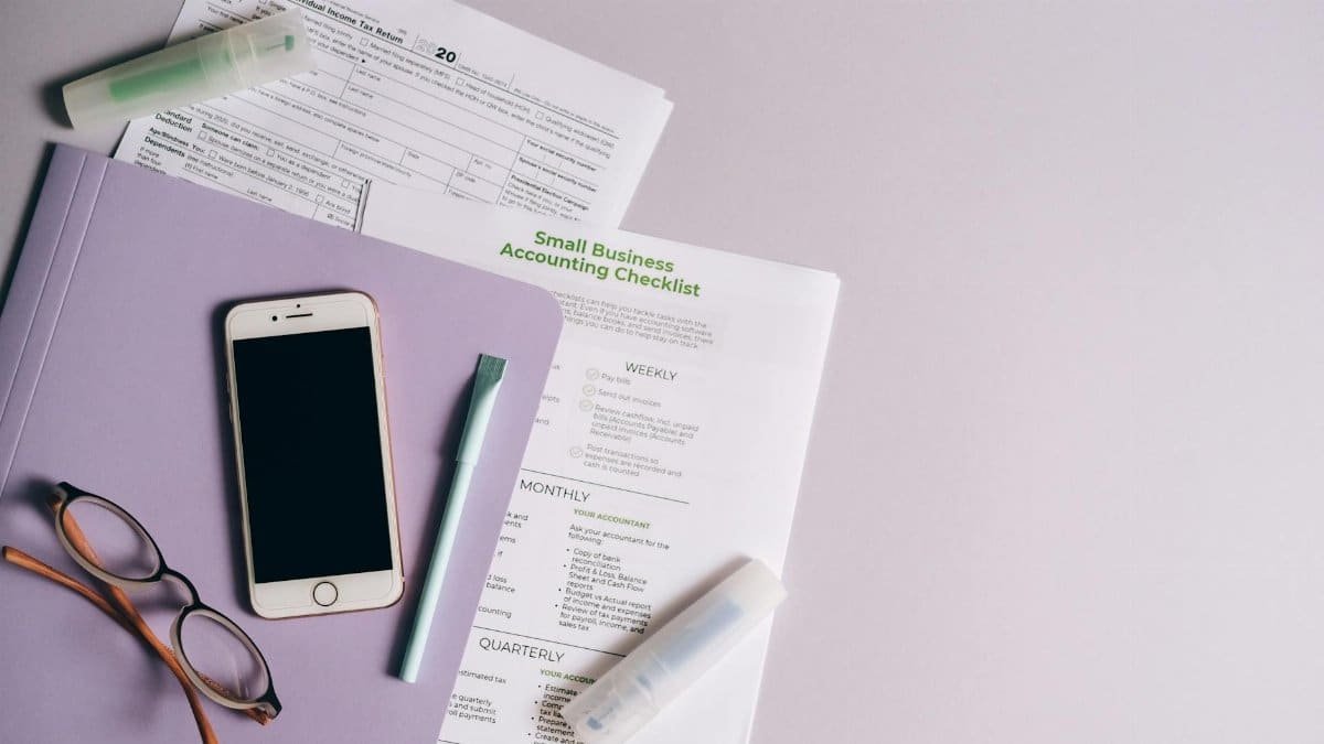 Flat lay of accounting documents, smartphone, and glasses on a desk.