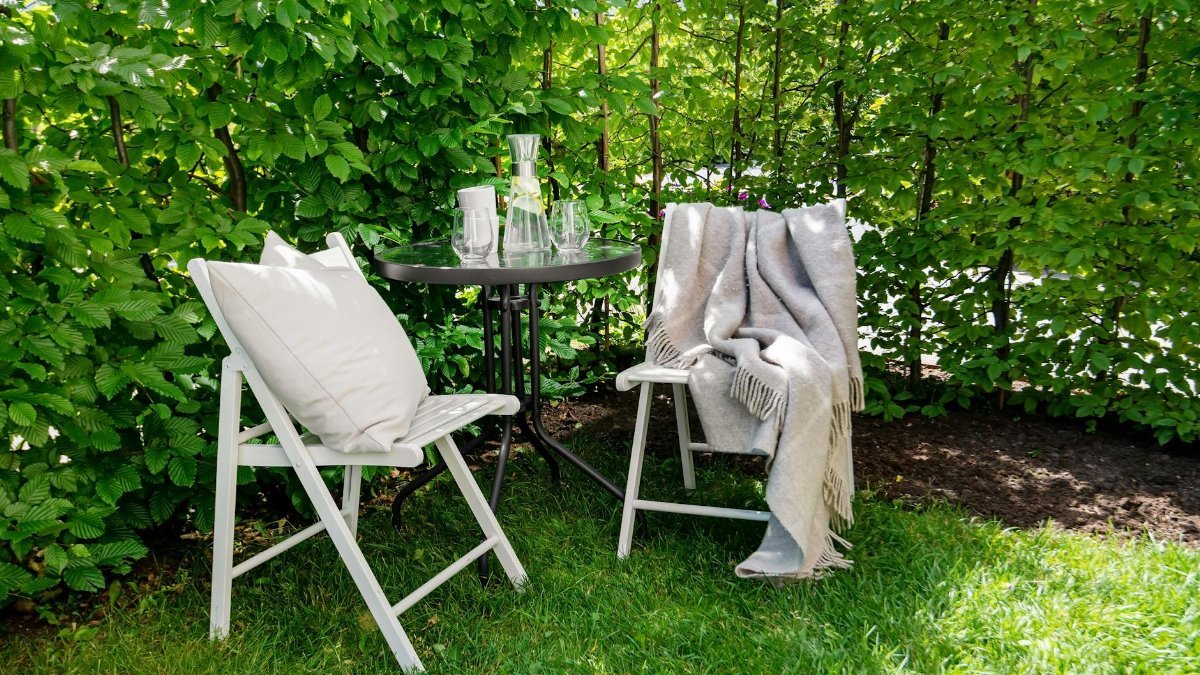 Relaxing outdoor patio setup with chairs, table, and green garden backdrop.