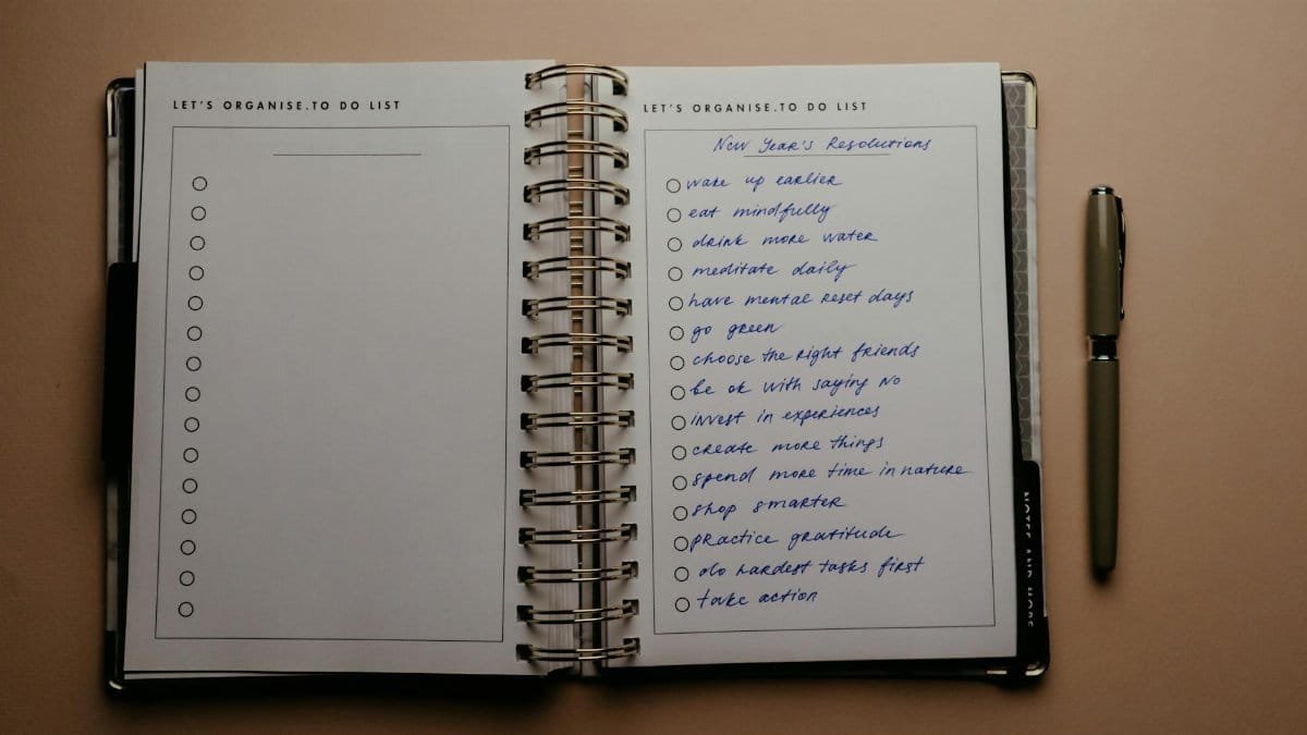 Open planner with New Year's resolutions, spiral binding, and pen on warm-toned background.