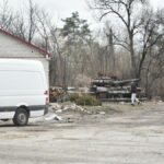 Scene of a war-torn area with an abandoned tank and van, illustrating the aftermath of conflict.
