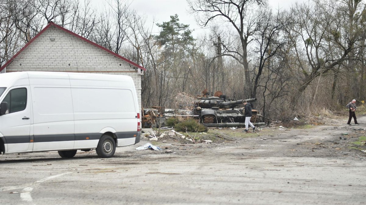 Scene of a war-torn area with an abandoned tank and van, illustrating the aftermath of conflict.