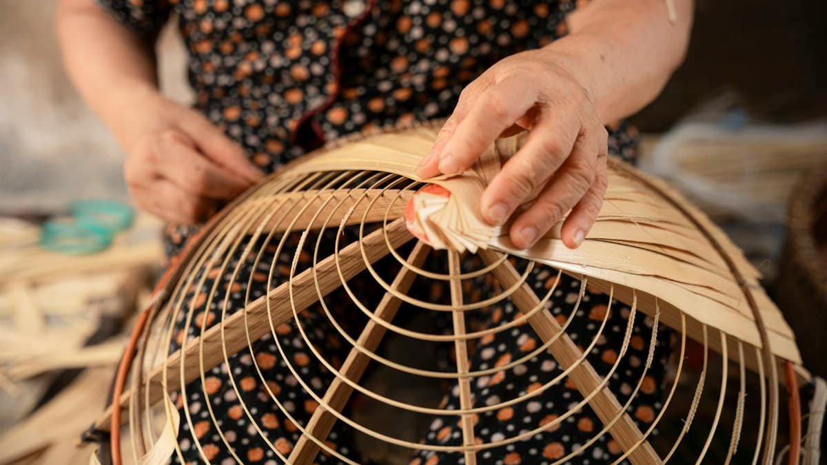 Close-up of a person weaving a traditional Vietnamese bamboo basket by hand.