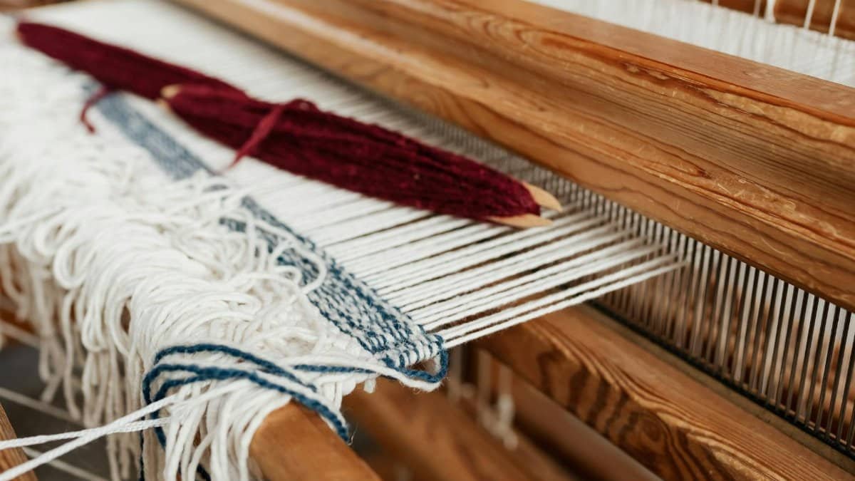 Detailed shot of a wooden loom with white and blue threads in a weaving process.