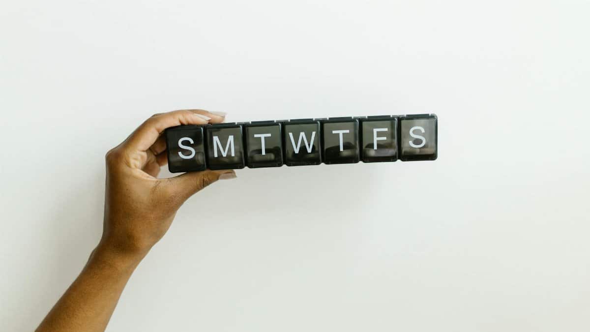 Close-up of a hand holding a pill organizer for daily medication, labeled with days of the week.