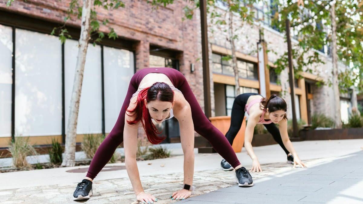Two women performing dynamic stretches outdoors, showcasing fitness and strength.