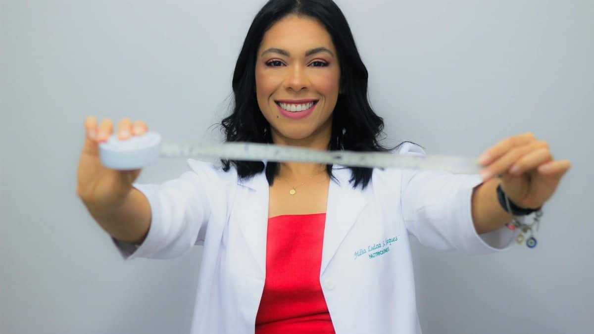 Cheerful nutritionist smiling broadly while holding a measuring tape, symbolizing healthy lifestyle and wellness.