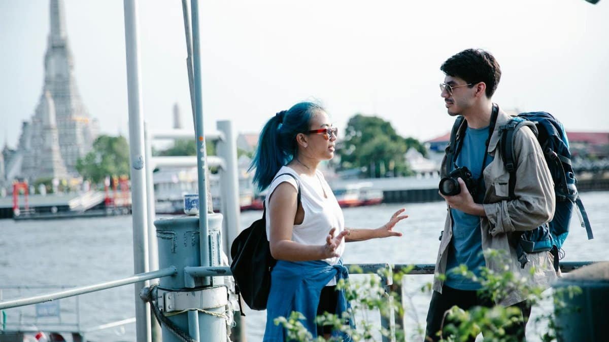 Travelers at Wat Arun, Bangkok, enjoy a conversation by the river. Perfect for travel themes.