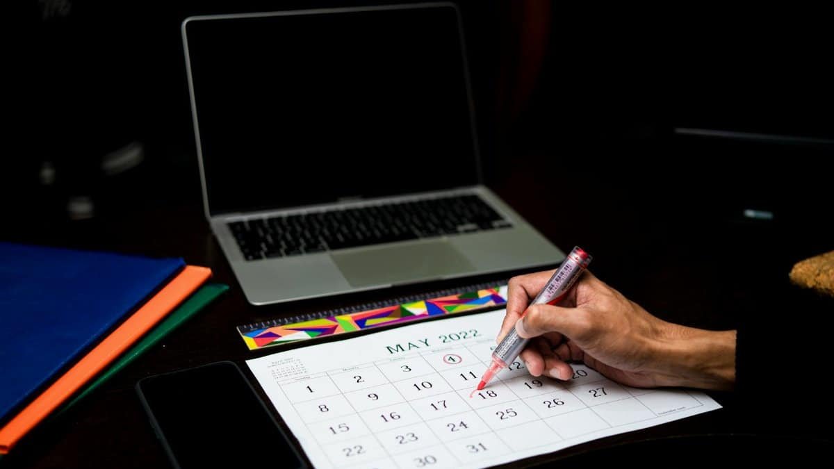 A person plans on a calendar at a desk with a laptop and phone, May 2022.