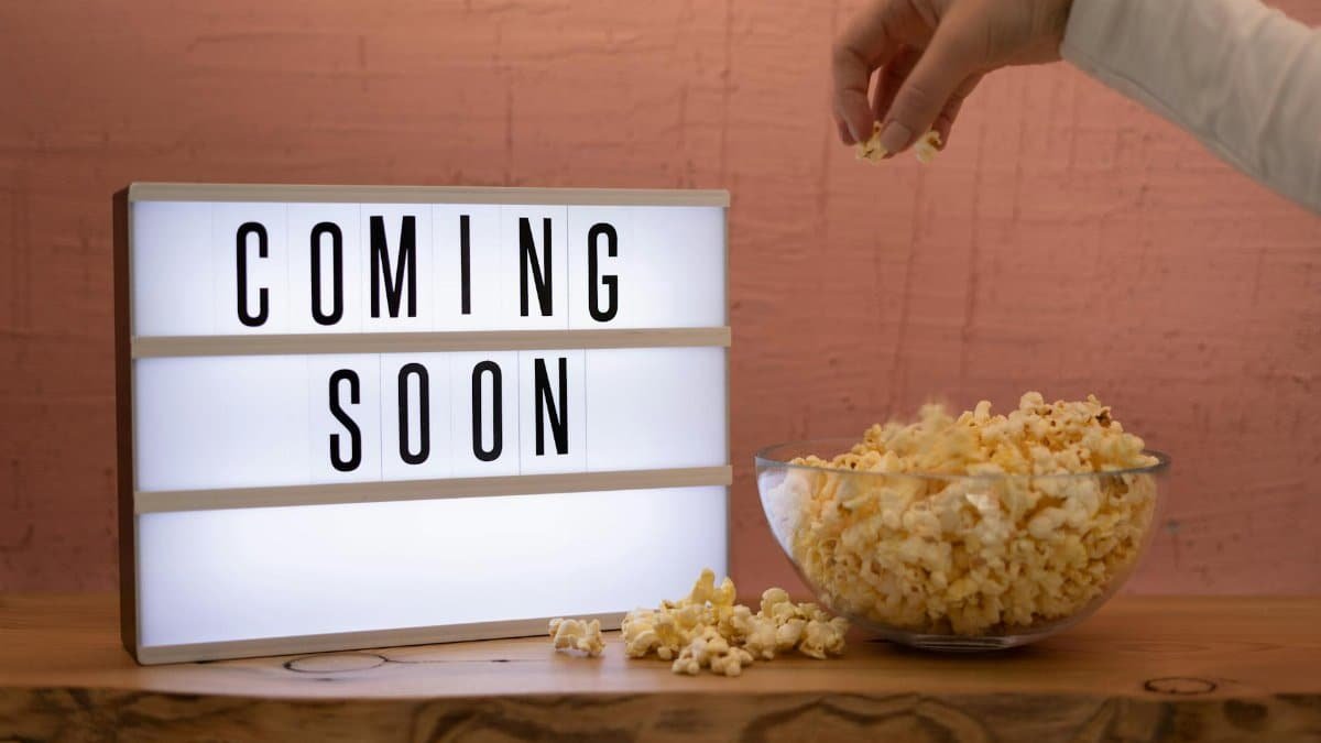 A hand reaching for popcorn next to an illuminated 'Coming Soon' sign, creating a cinematic feel.