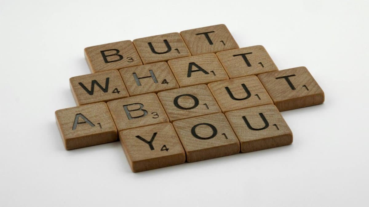 Close-up of wooden Scrabble tiles spelling 'But What About You' on a white surface.
