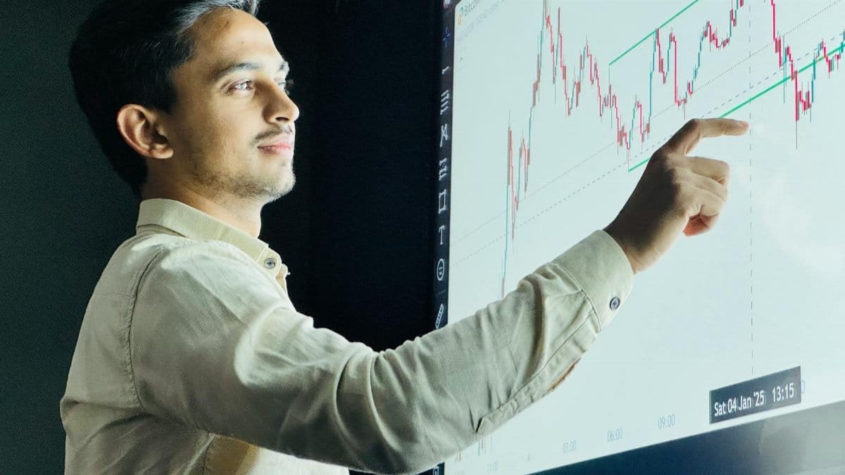 Man analyzing stock market graph on a digital board with a focused expression.