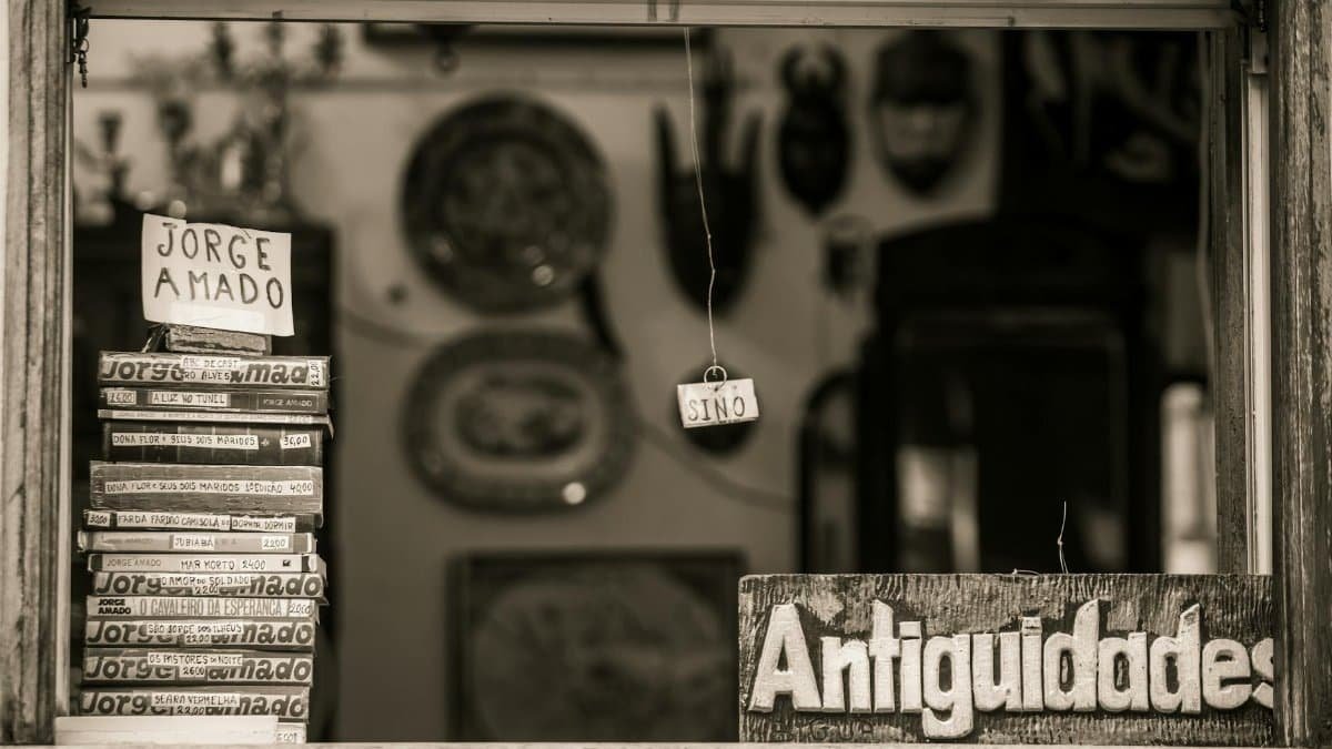 Black and white photo of a vintage shop featuring Jorge Amado books and 'Antiguidades' sign in Bahia, Brazil.