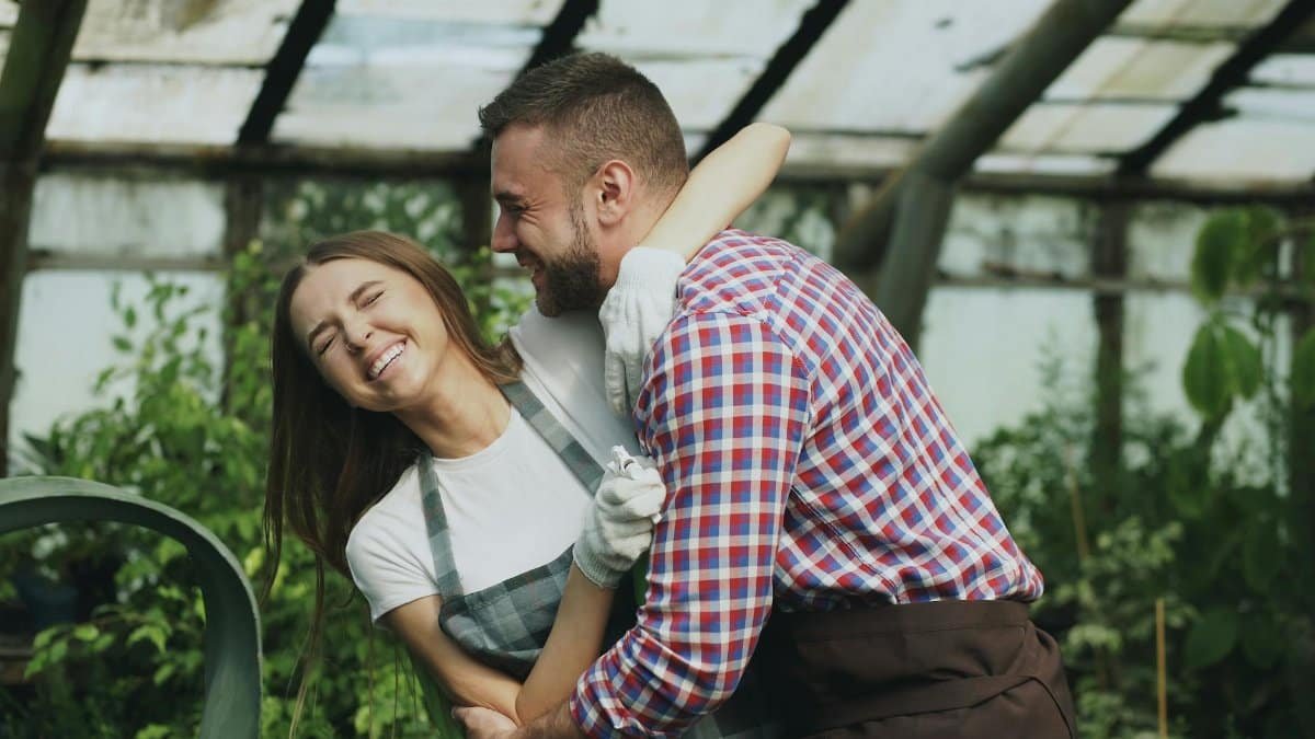 Cheerful couple enjoying gardening together in a greenhouse environment.