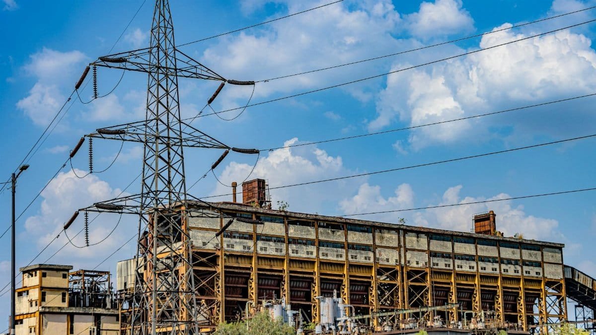 Photograph of an abandoned industrial building with a power line tower against a blue sky.