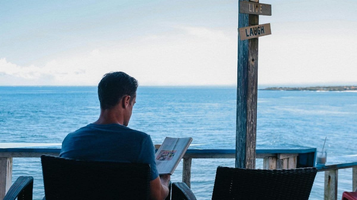 A man relaxes with a book overlooking the ocean in Bali, enjoying leisure time.