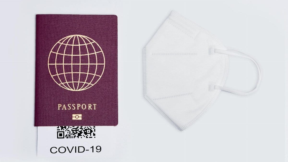 Flat lay of a travel passport, face mask, and COVID-19 QR code on a white surface, symbolizing pandemic travel.