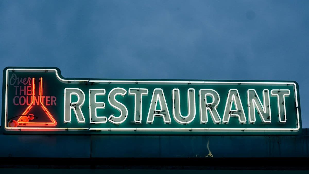 Gleaming neon restaurant sign with vibrant colors against a dusk sky, perfect for urban nightlife themes.