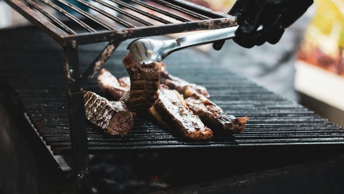 A person grilling delicious beef over a barbecue outdoors in Recife, Brazil.