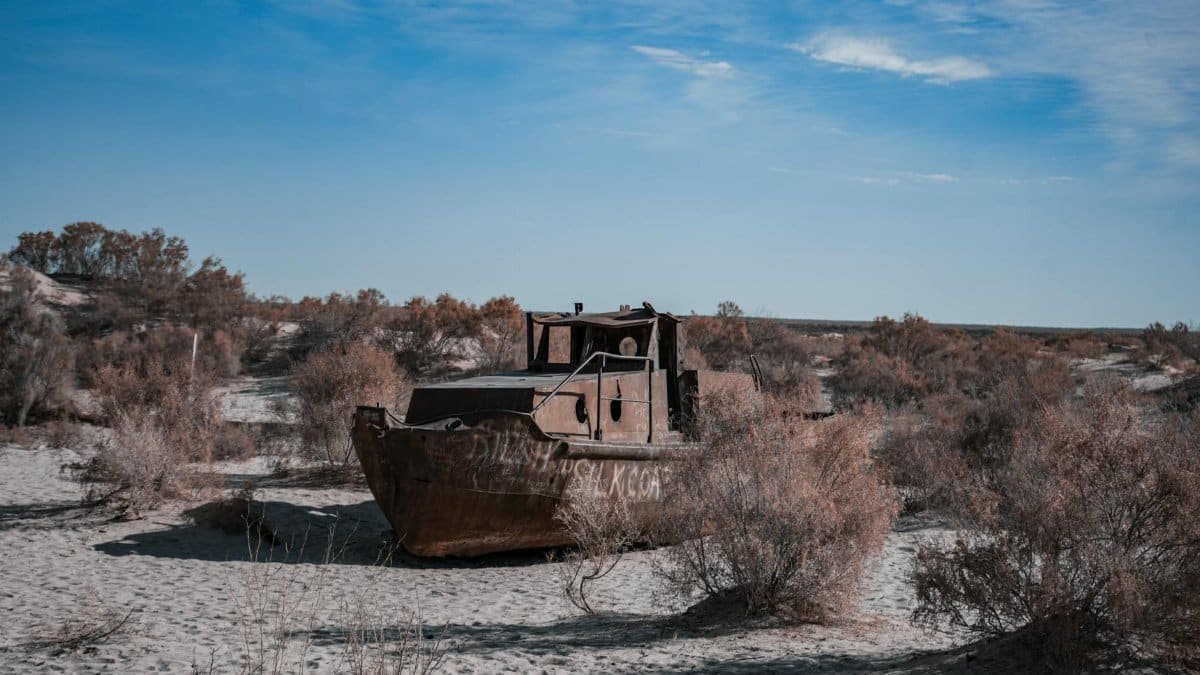 An old, rusting ship stranded on the desert sands of the Aral Sea under a bright blue sky.
