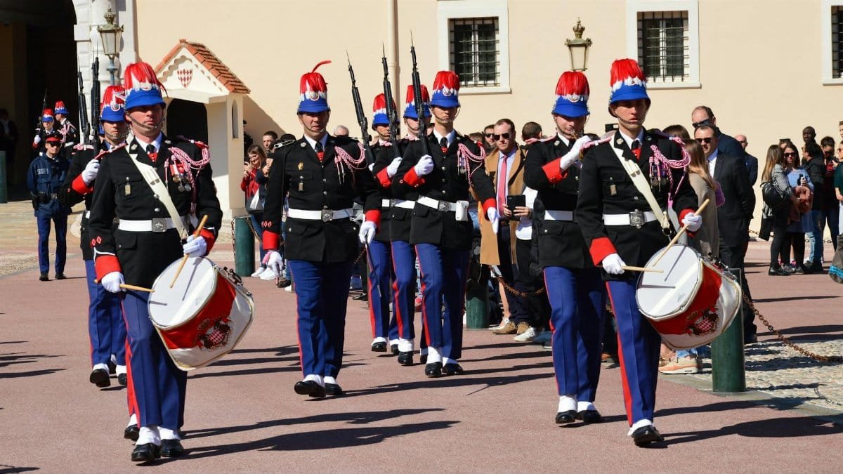 Royal guards in vibrant uniforms parade with drums during a ceremonial march outdoors.