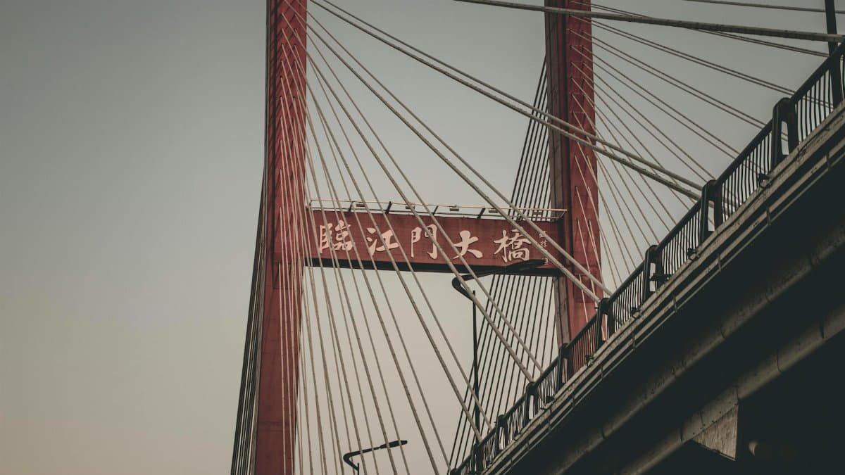 A modern suspension bridge captured from a low angle during twilight, showcasing its red pillars and cables.