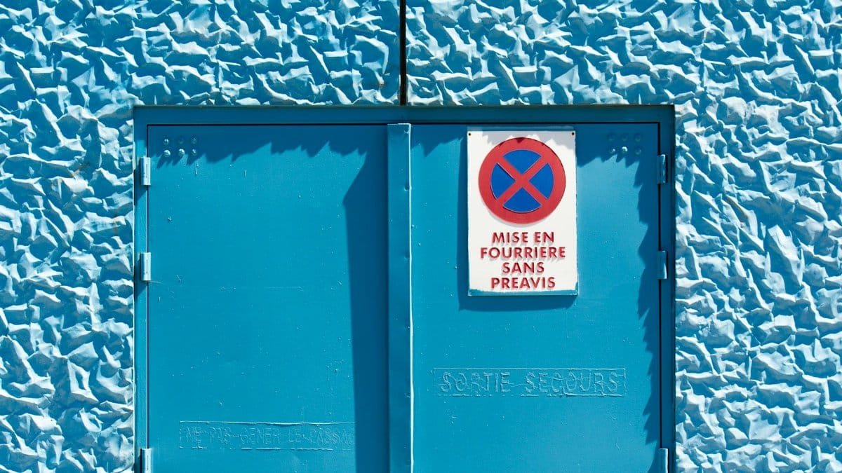 Bright blue textured wall with warning sign and exit door.