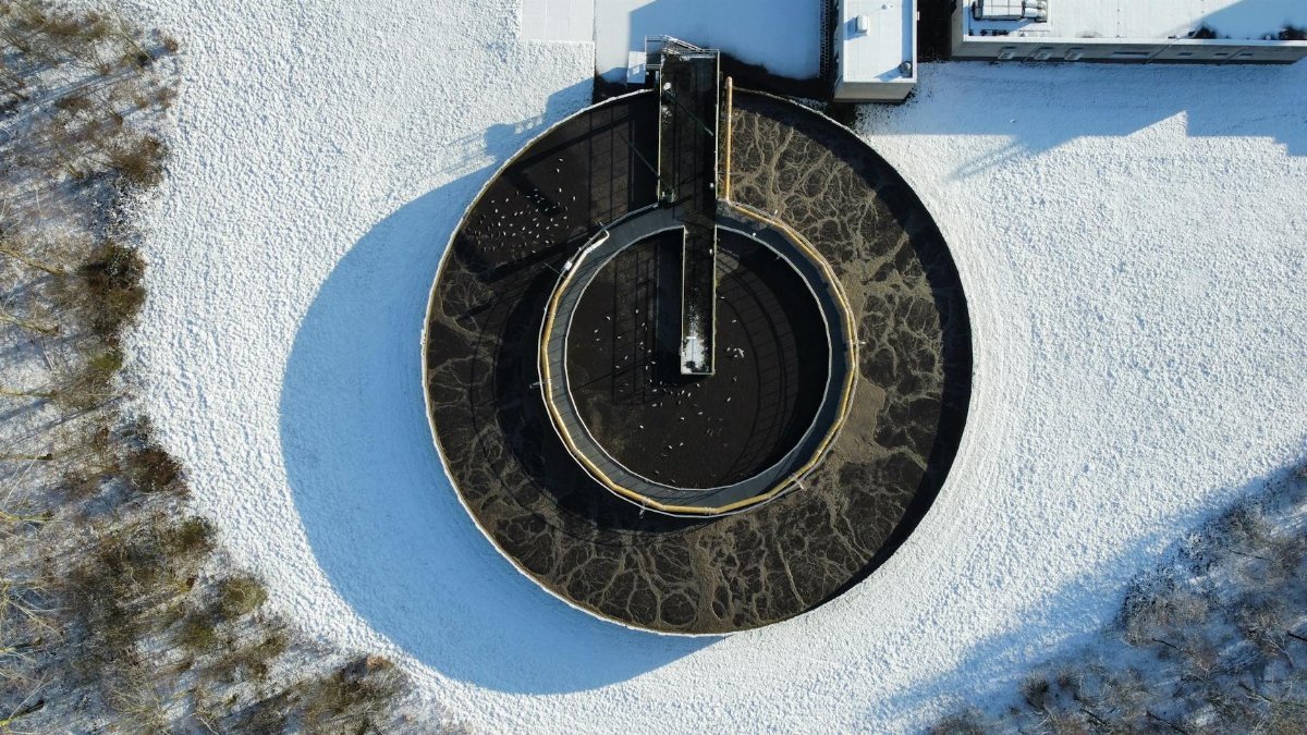 Drone shot of a circular wastewater treatment plant surrounded by winter snow.