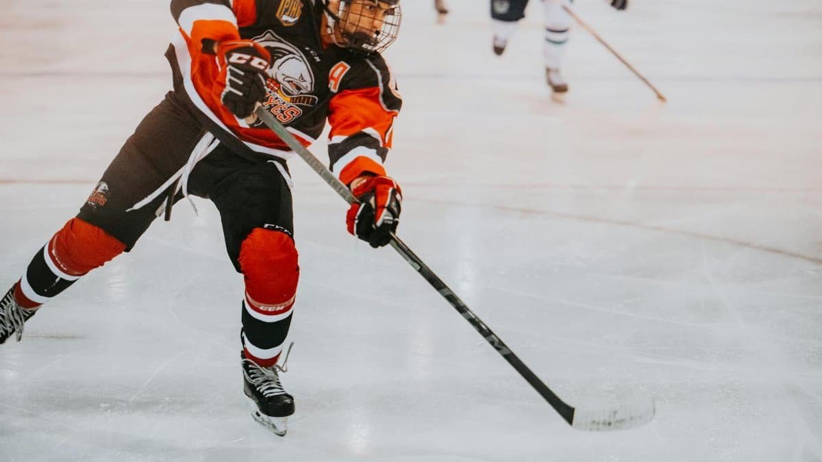 A male ice hockey player in full gear skates aggressively on ice during a game.