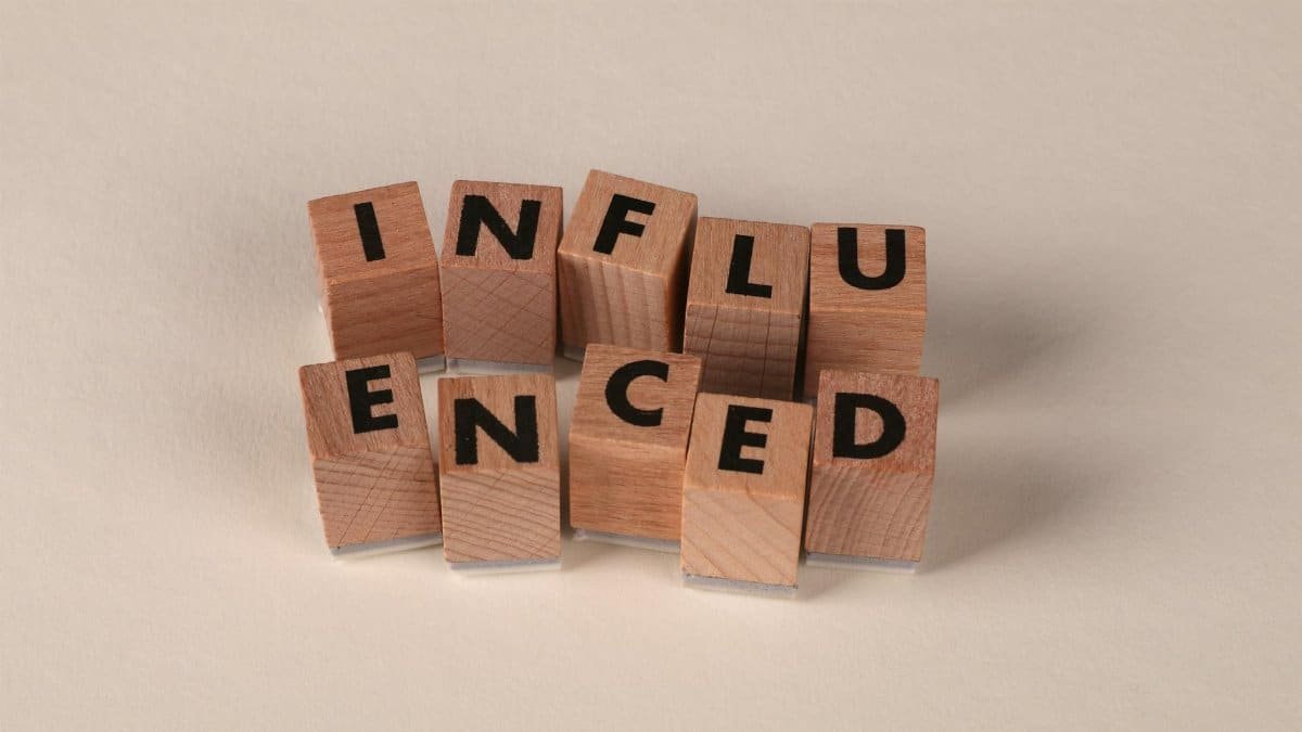 Wooden letter blocks arranged to spell 'Influenced' on a neutral beige surface.