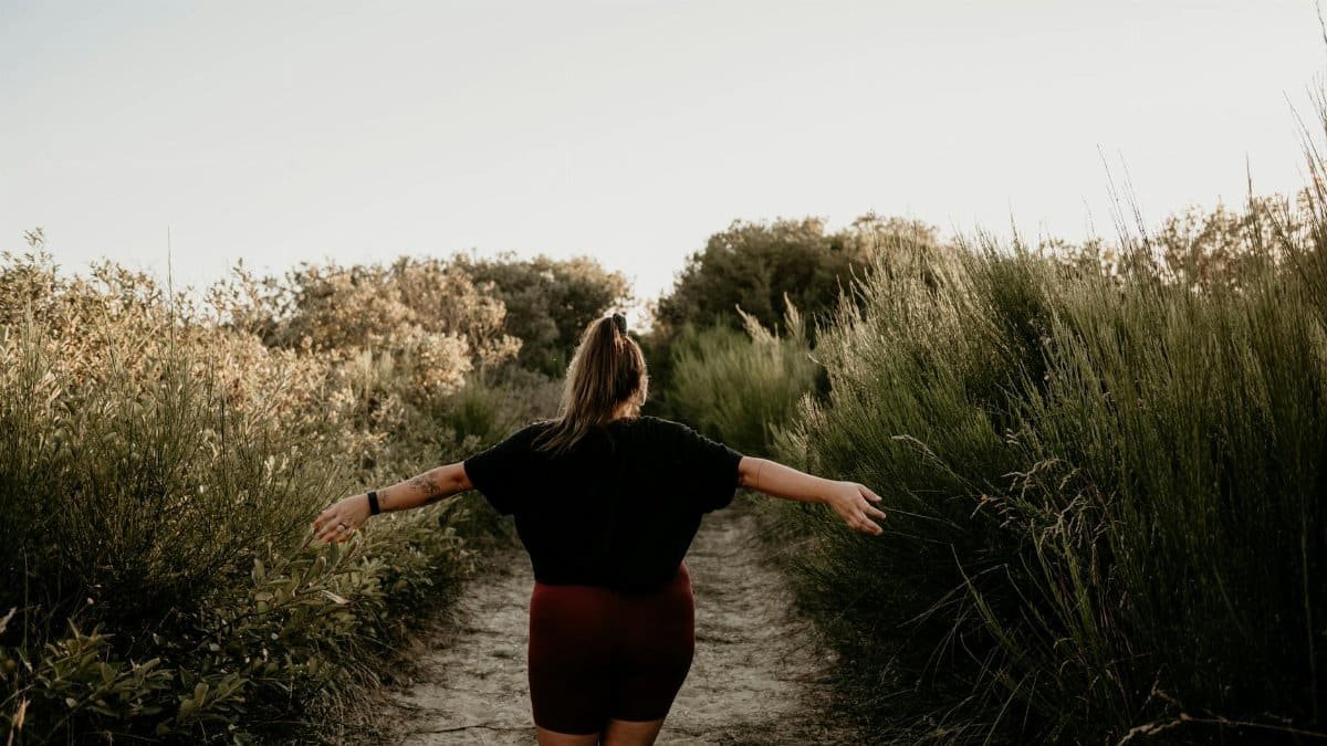 Back view of a woman walking on a rural path in summer with tall grass around.