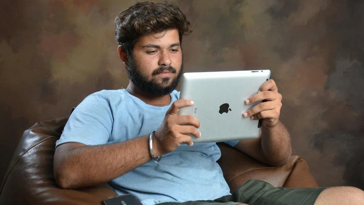 A man in a blue shirt sits in a comfortable armchair using a tablet, creating a casual and relaxed atmosphere.