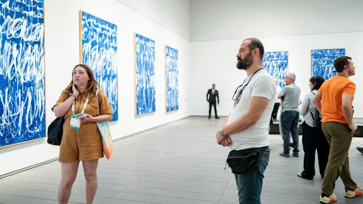 Visitors in an art gallery engaging with blue abstract artworks. Captured indoors with contemporary art, diverse visitors enhancing the scene.