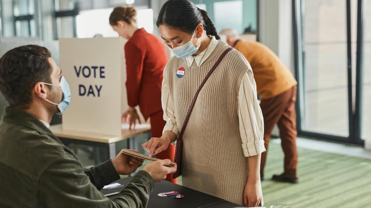 Voters casting ballots indoors on Election Day, wearing masks and using tablets for contactless voting.