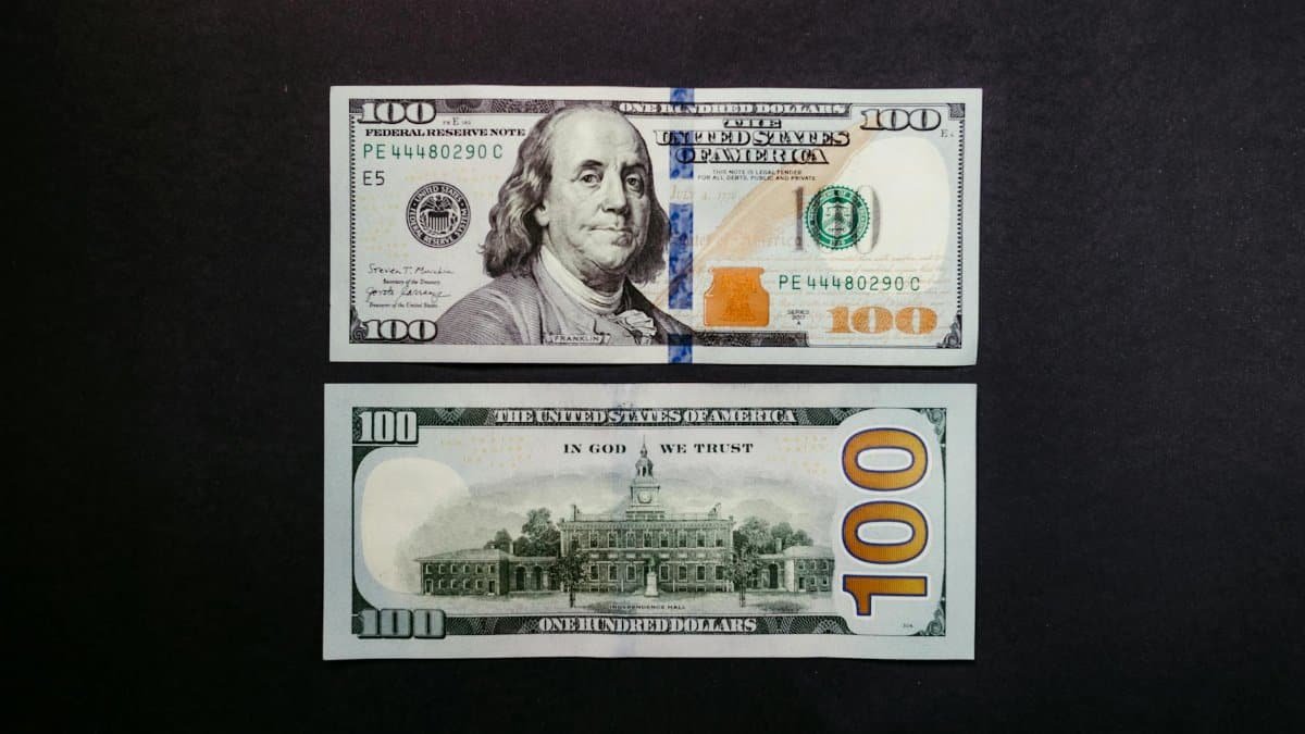 Detailed photo of US hundred dollar bills showing Benjamin Franklin and US currency design.