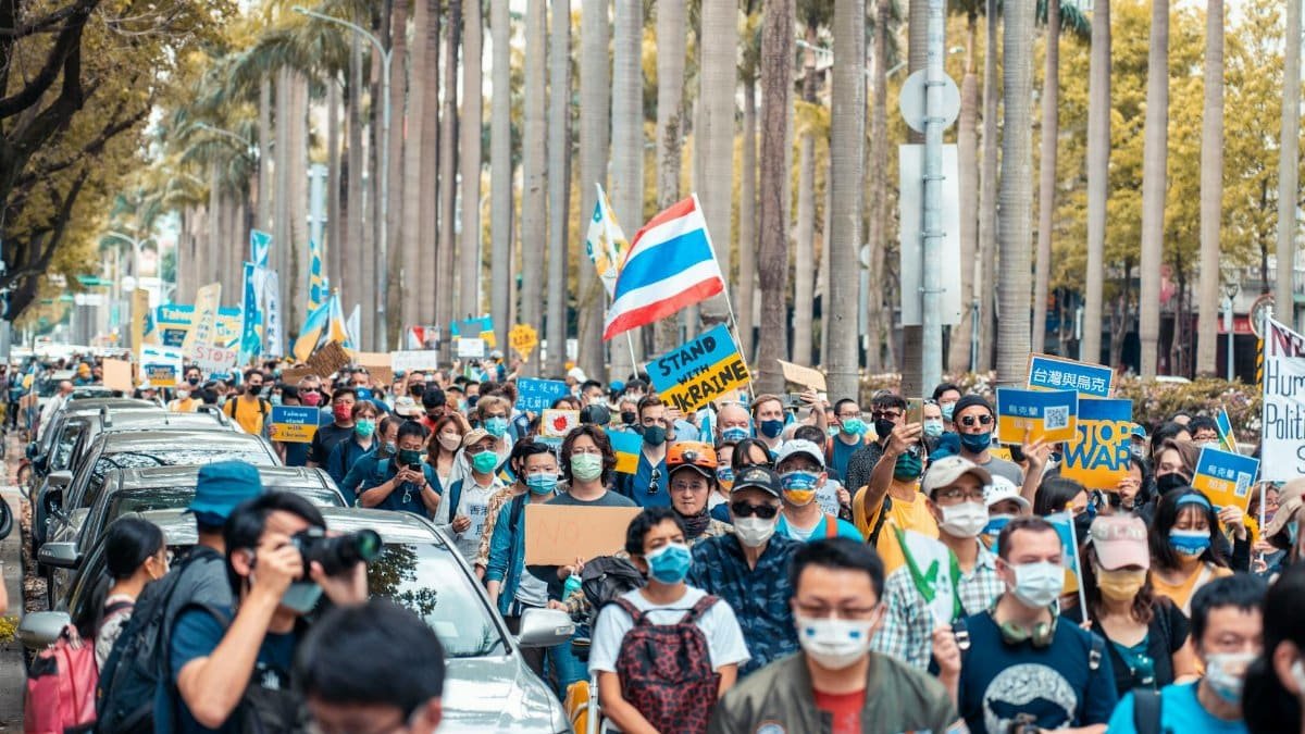 Crowd of people at city rally holding signs against war, demonstrating social issues.