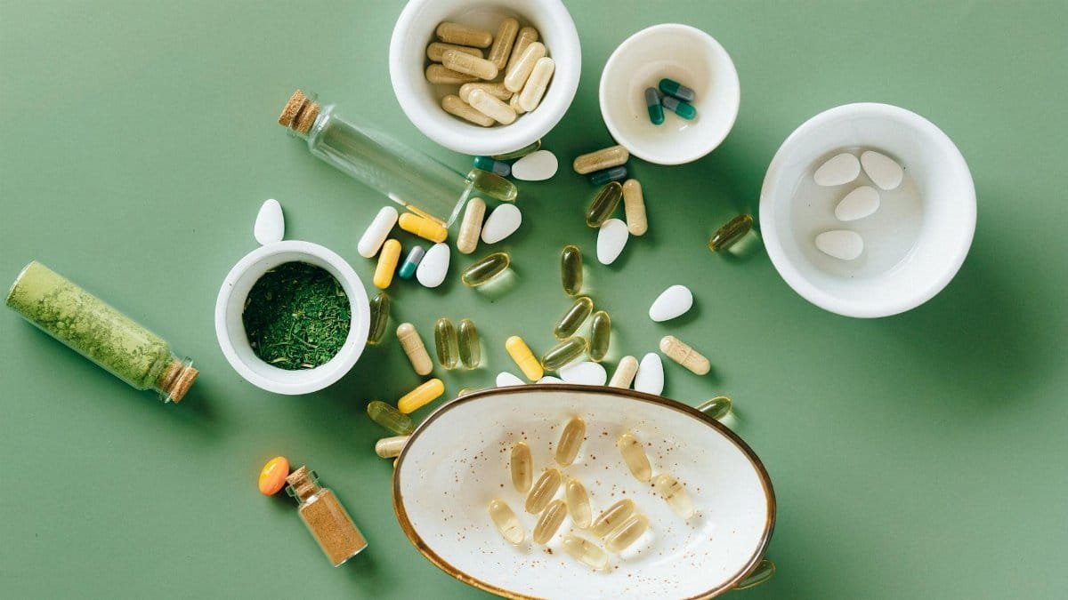 Top view of various herbal and pharmaceutical supplements in ceramic bowls on a green background.