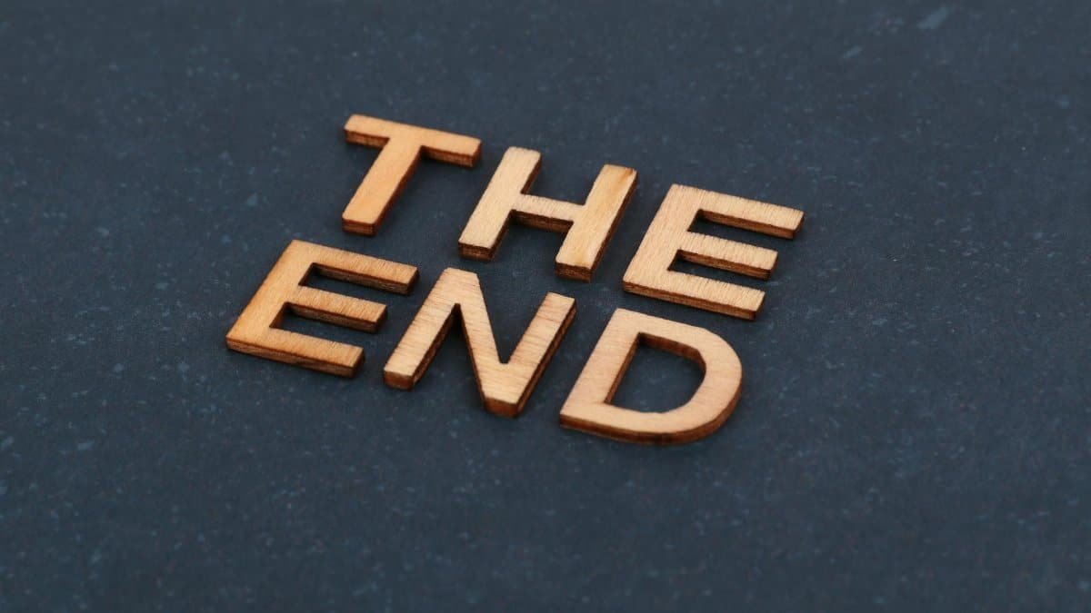 Wooden block letters spelling 'The End' on dark surface, artistic composition.