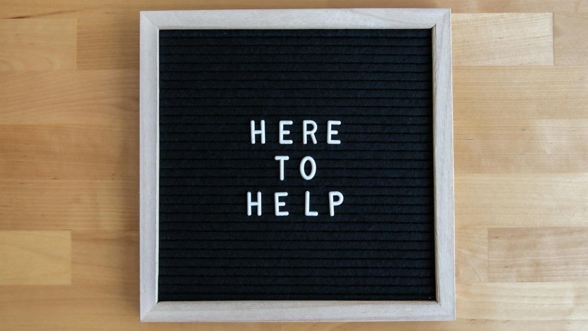 Black letter board with white text 'Here to Help' on a wooden background.