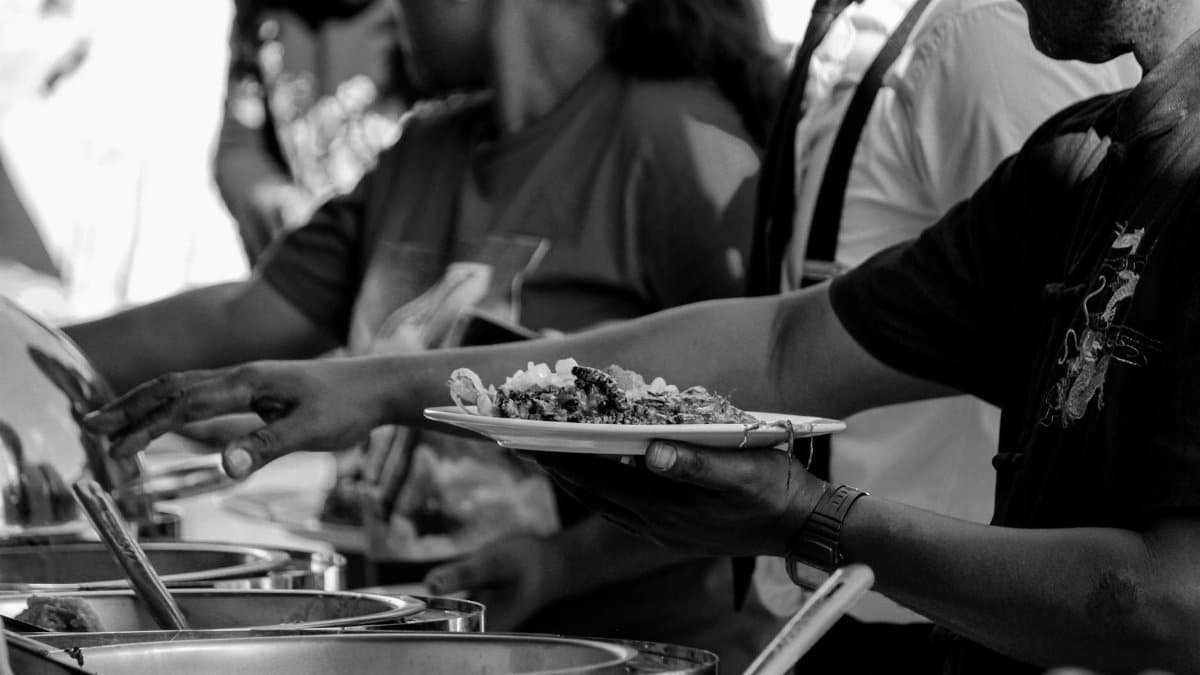 Black and white of crop anonymous group of people serving food in plates while visiting smorgasbord