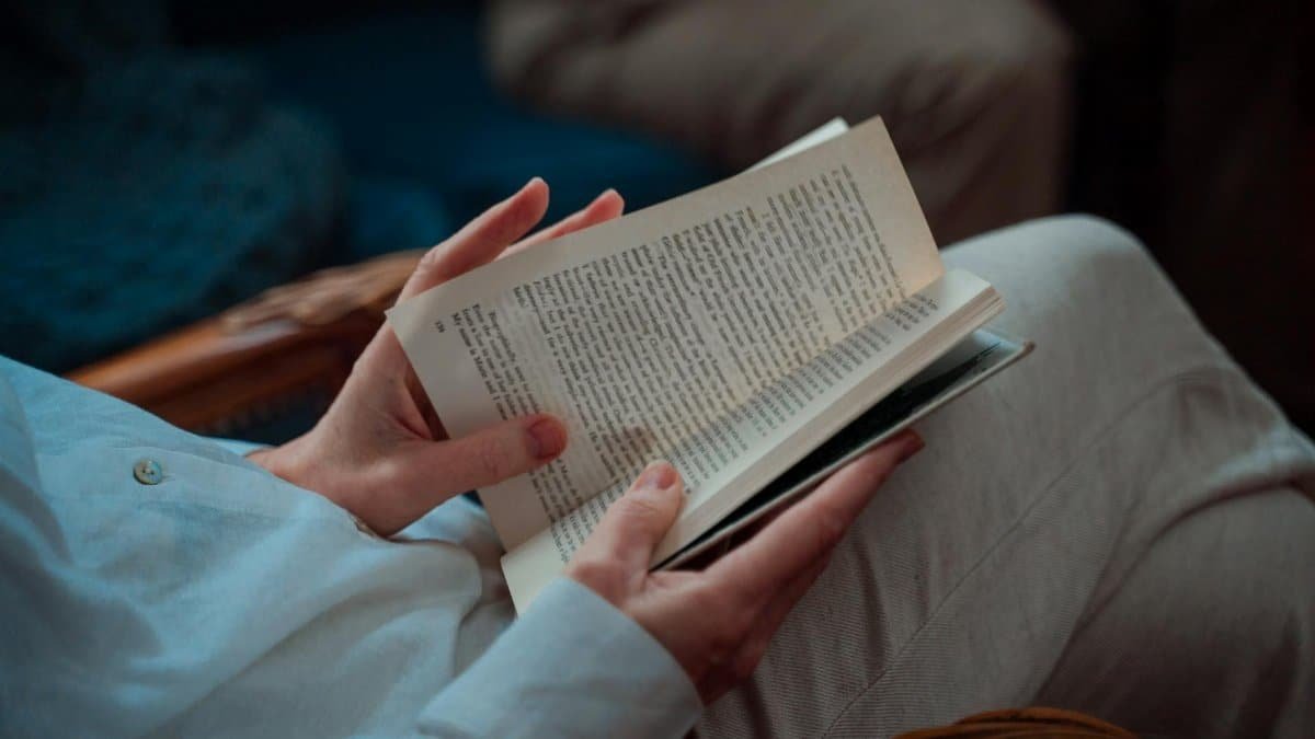 A person leisurely sitting and reading an open book indoors, capturing the essence of relaxation.